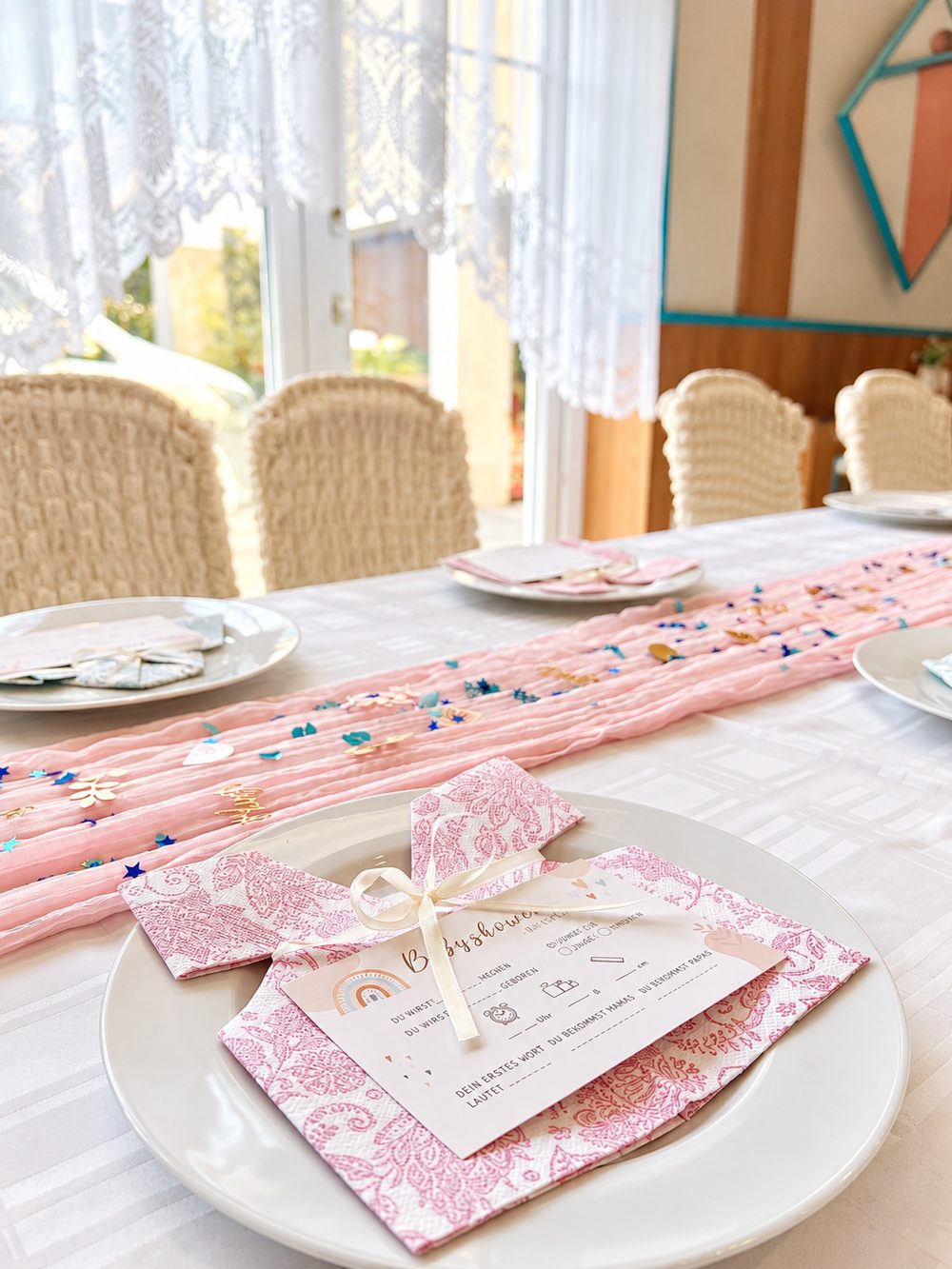 Babyshower-Tischdeko mit rosa Tischläufer, Serviette als Babyhemd und Spielkarte